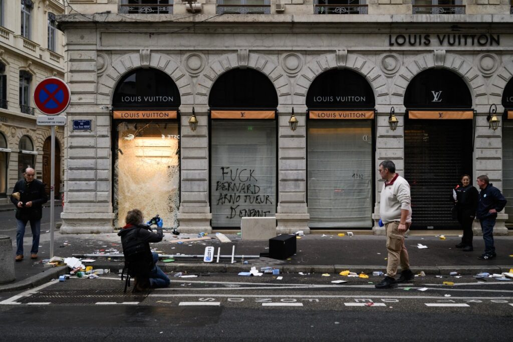 Ein Polizist fotografiert am 18. Oktober 2026 in Lyon (Mittelostfrankreich) die zerbrochene Schaufensterscheibe eines Louis-Vuitton-Geschäfts. (Foto: JEFF PACHOUD / AFP)