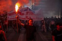 Ein Demonstrant hält eine Leuchtfackel in der Hand, während Studenten, Lehrer und Beamte an einer Kundgebung in Athen am 21. Oktober 2026 teilnehmen, um gegen die hohen Lebenshaltungskosten zu protestieren. (Foto: Angelos TZORTZINIS / AFP)